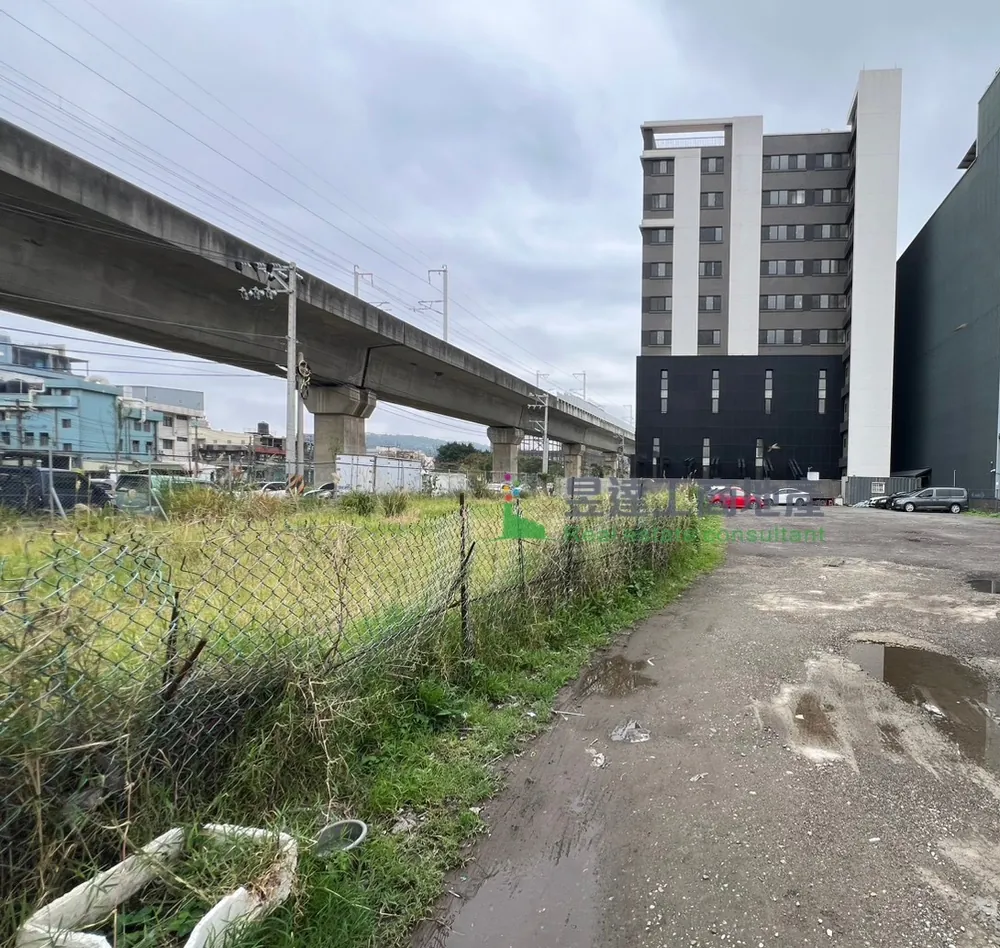 南崁乙種工業區土地一帶現況示意：沿著鐵絲網的碎石通道，右側是停車與鐵皮棚架，遠處是多層廠房與大樓