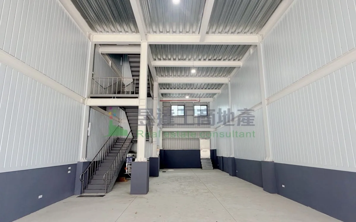 中壢鋼構兩層廠房一樓挑高空間實景：鋼骨樑柱，左側室內樓梯通往二樓